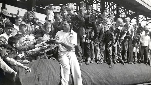 Sammy Baugh, quarterback for the Washington Redskins, attending to an admiring crowd of young fans and autograph seekers during height of his career.