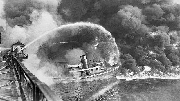 Nov. 3rd, 1952. Fireman on railroad bridge apply water to tug boat ‘Arizona’ amidst flames from the burning Cuyahoga River. Original United Press photo caption reported that “fire started in an oil slick on the river, swept docks at the Great Lakes Towing Co., destroying three tugs, three buildings and the ship repair yards.” (photo mistakenly used by Time magazine as 1969 fire).