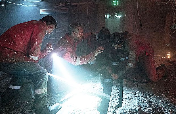 Mark Wahlberg’s Mike Williams character shown with flash light and crow bar at left, and Mr. Jimmy next to him, trying to free trapped worker whose leg is stuck and severely injured between damaged deck flooring.