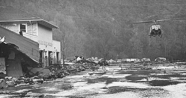 A helicopter hovers over one location in the Buffalo Creek valley, surveying the damage in the aftermath of the coal dam failures and devastating flood of February 26, 1972. Note mud lines on the building at left, marking flood level.
