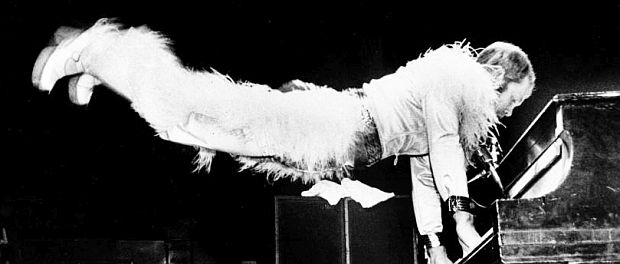 Elton John in concert during the 1970s, doing one of his flying handstands, extending out from the piano keyboard, typically revving up the audience with his energetic performances. 