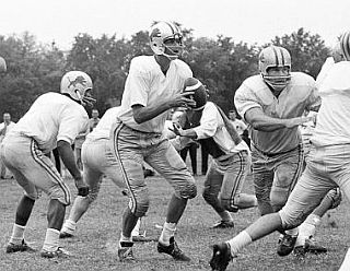 August 1963: George Plimpton, at center with ball, going through some practice drills at Detroit Lions camp, appears to be looking for a receiver with some trepidation.