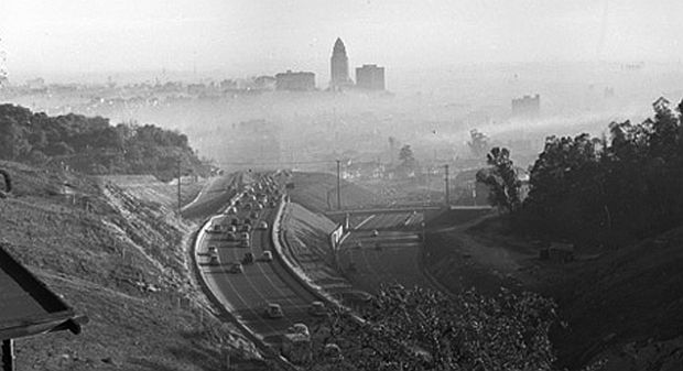 Early 1940s photo of highway leading into downtown Los Angeles, with smog forming over the city there, showing the tall landmark L.A. City Hall building at center in the distance. 