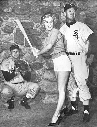Marilyn Monroe in 1951 publicity photo posing in a batting stance with Chicago White Sox players Joe Dobson and Gus Zernial.