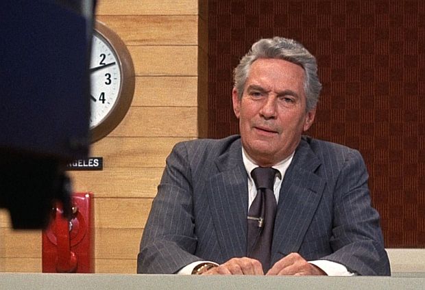 Howard Beale ( Peter Finch ), “grand old man of news” at UBS-TV, shown at his news desk in a more sedate pose than his later “angry man” broadcasts.  Still, during this broadcast he tells his audience he is bing fired for low ratings and on his next broadcast he will “blow his brains out” on live TV.