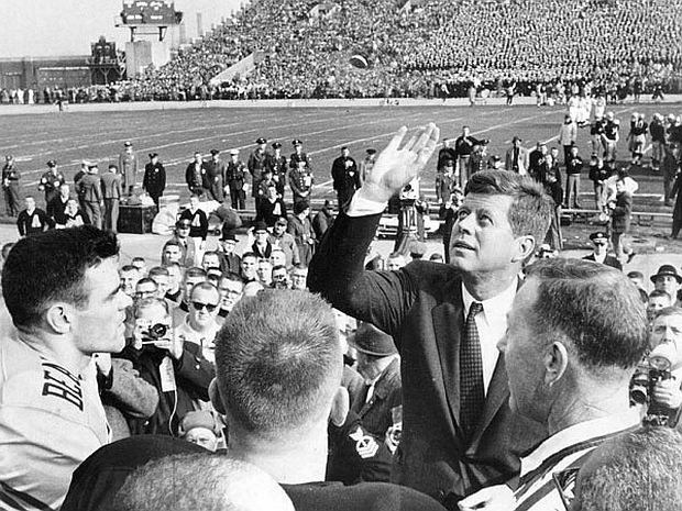 President John F. Kennedy, making coin toss, at earlier Army-Navy game in Philadelphia, PA, as representative from Army and Navy teams and others look on. Photo, Philadelphia Inquirer.