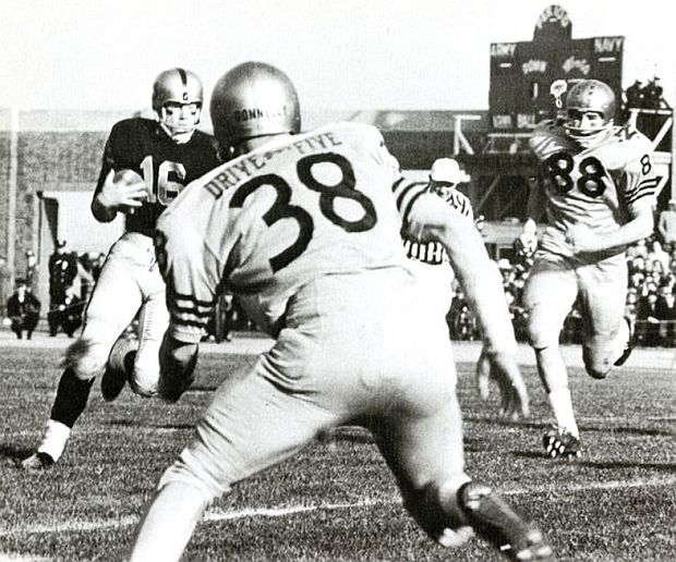 Photo of early play in 1963 Army-Navy game shows Navy QB, Rollie Stichweh on the move as Navy defenders zero in on him, with their “Drive-For-Five” jersey labeling added as extra incentive and taunt at Army players. 