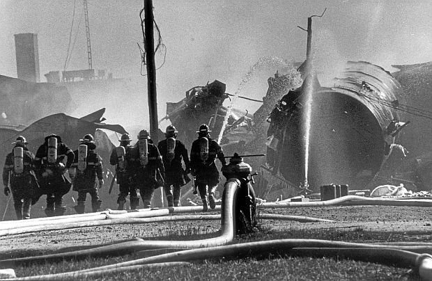 At the November 1979 scene of the Mississauga train derailment, water streams continue to soak the still-burning rail cars as firefighters wearing breathing equipment head for work on the wreckage. Jack Dobson / The Globe and Mail