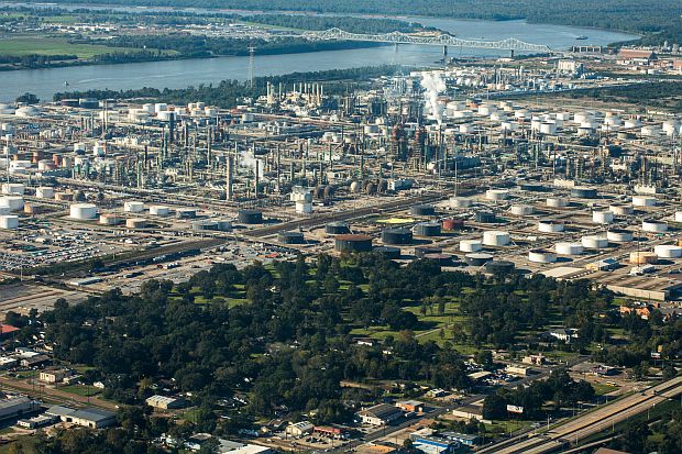 Photo of the ExxonMobil Baton Rouge, LA refinery, looking west over Mississippi River and showing portions of Standard Heights residential area in the foreground, increasingly part of a greenbelt program that Exxon initiated to buy out nearby neighbors. Photo, David Hanson, “Neighbors of the Fence,” BitterSoutherner.com, January 19, 2016.