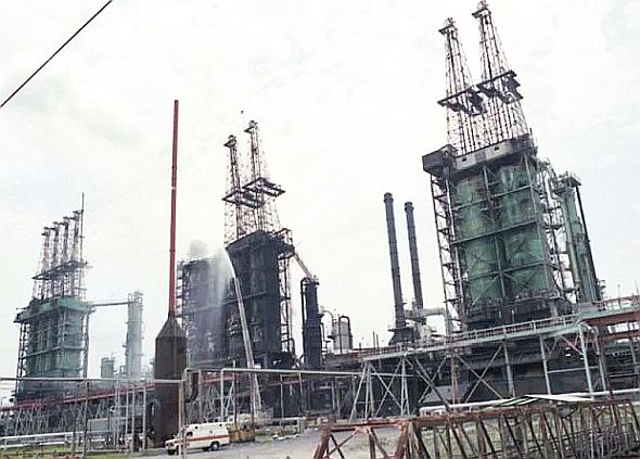 1990s photo of Exxon Baton Rouge refinery with 3 coker units, the size of which – for perspective – can be roughly compared to the small white truck / ambulance in the lower left foreground. Source, The Advocate newspaper.